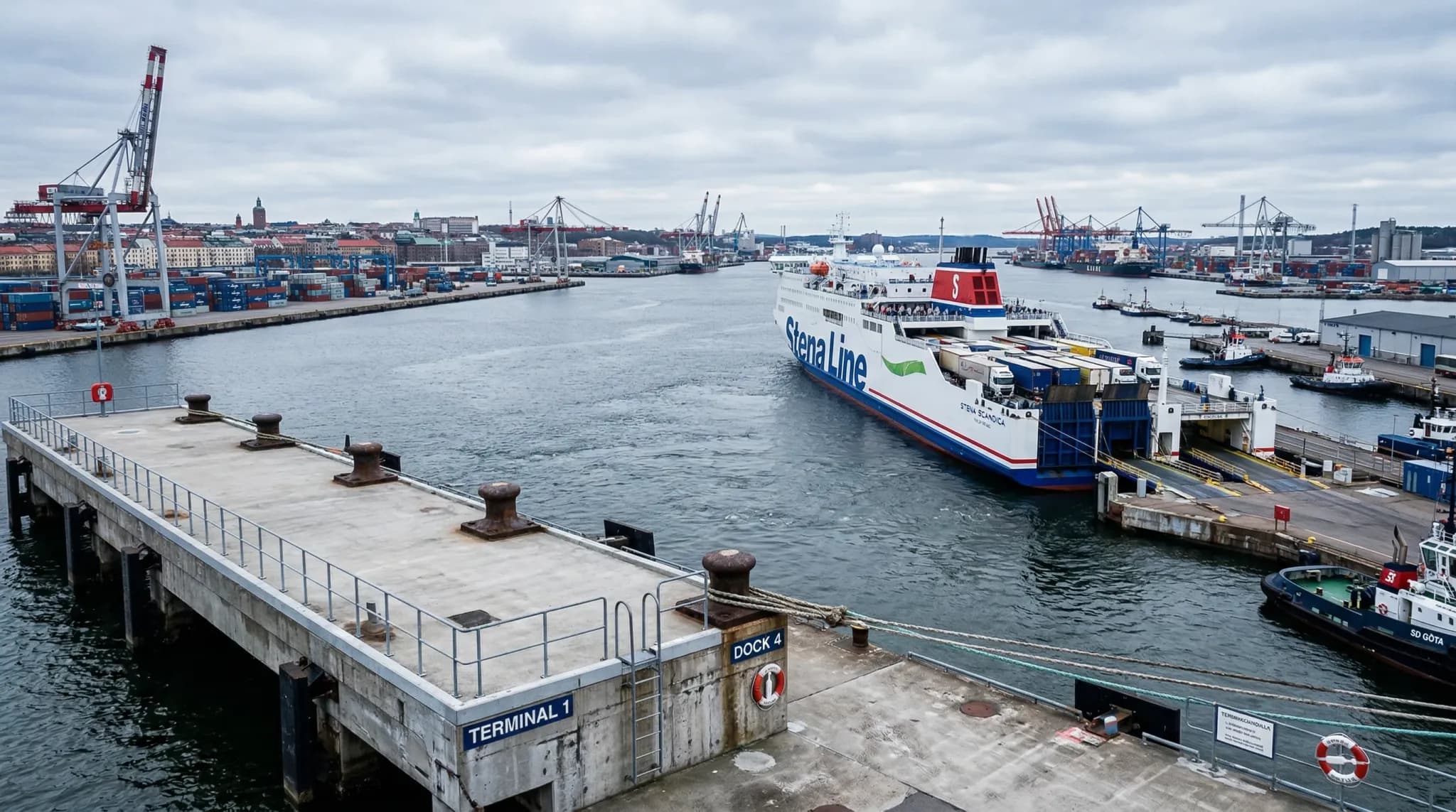 A wide-angle photorealistic shot of a large commercial harbor in Northern Europe under a soft, overcast sky. The foreground shows a clean concrete pier and weathered mooring bollards, with a large tra
