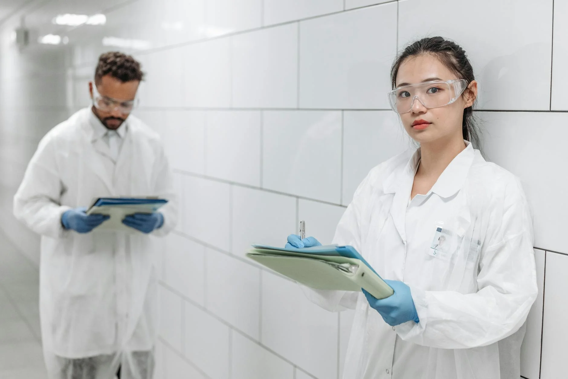 Two scientists in lab coats conducting research in a modern laboratory hallway.