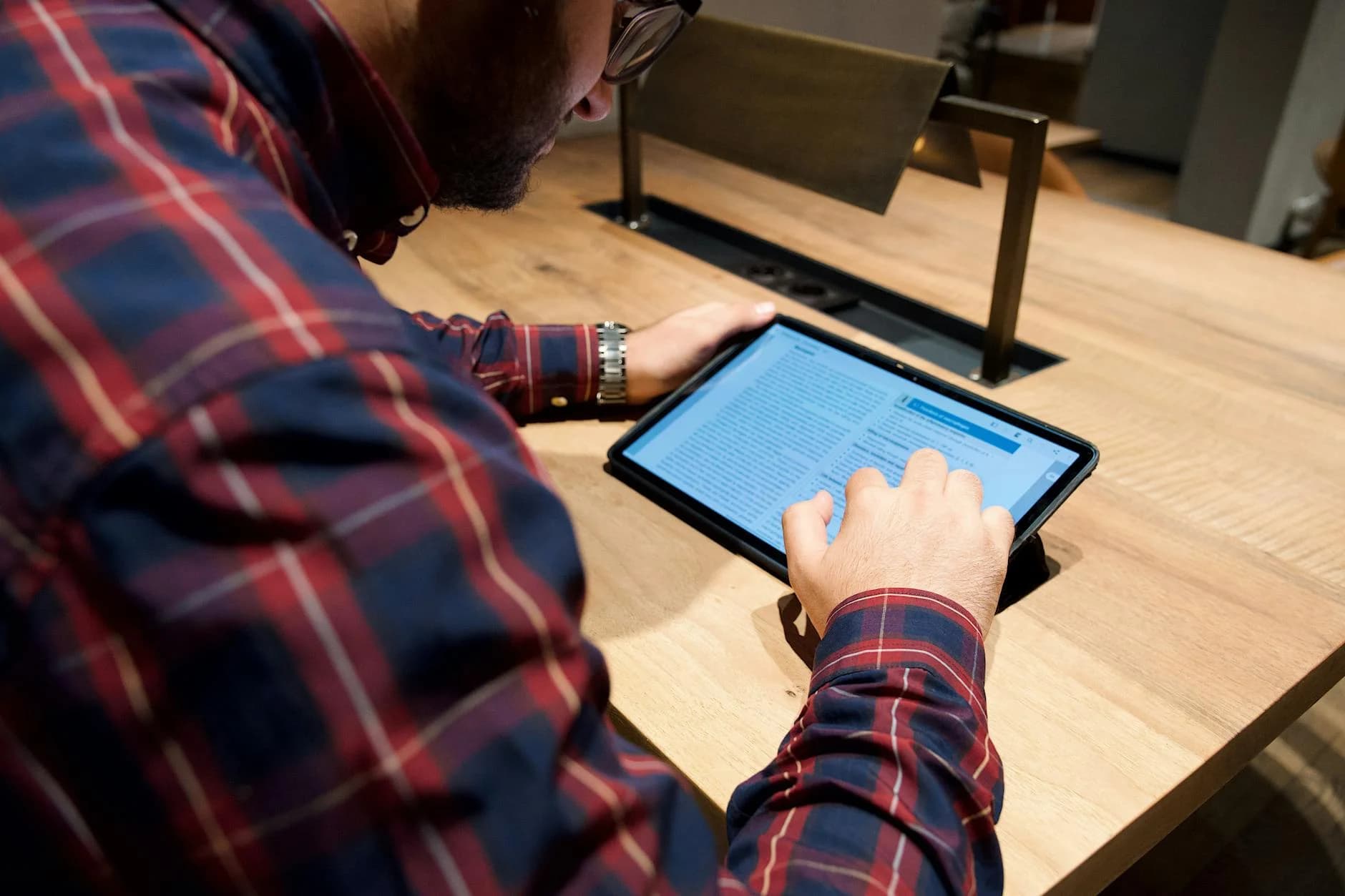 Close-up of a man using a tablet on a wooden table indoors.