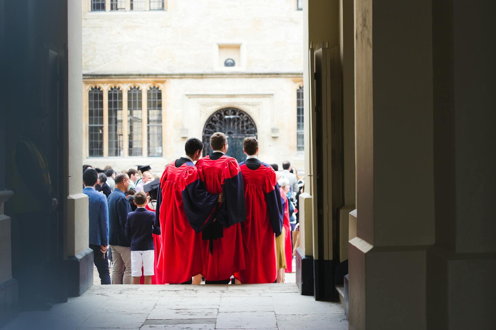 Back view of a graduation ceremony outdoors with students in red gowns gathering.
