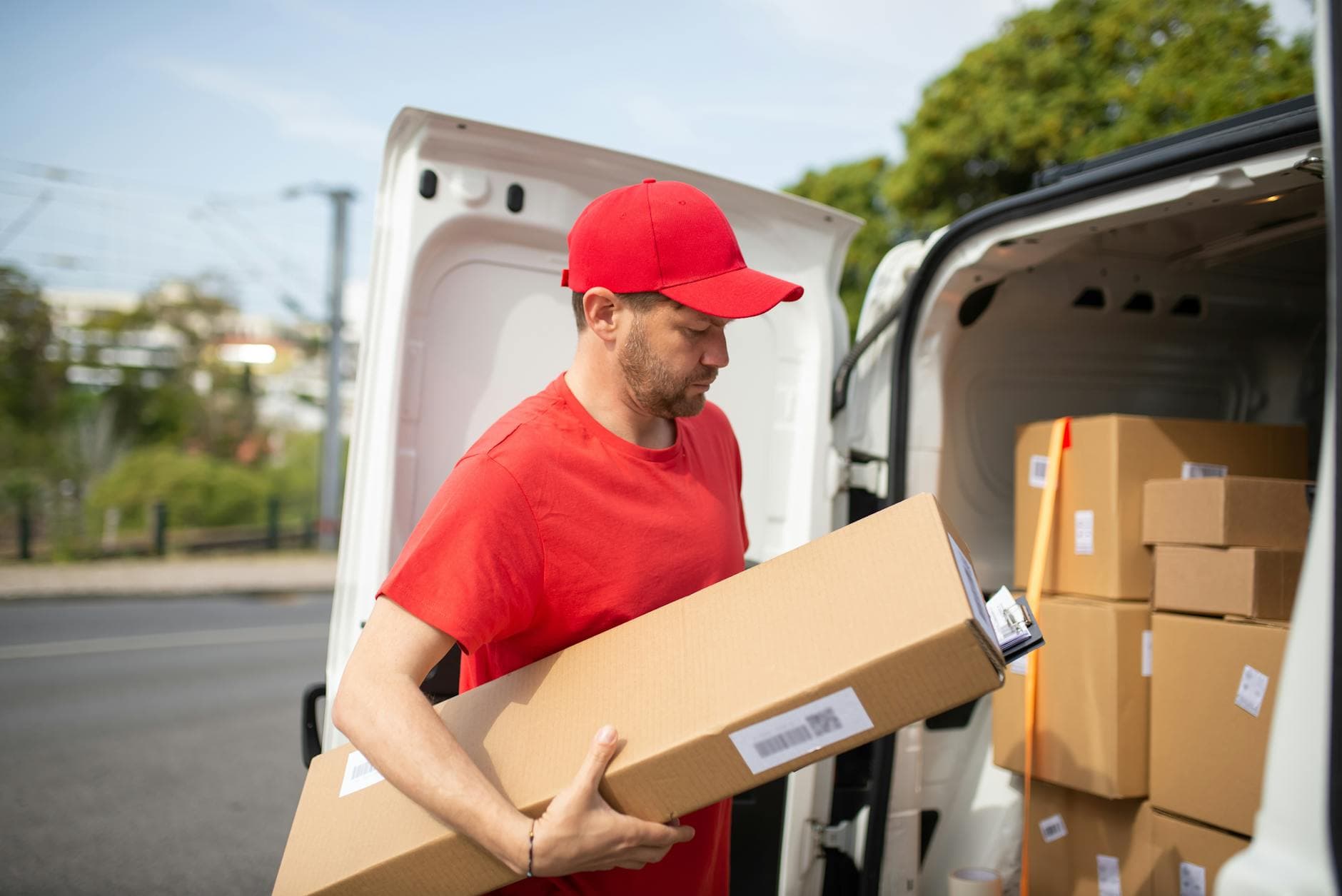 Courier in red uniform unloading packages from a delivery van on a sunny day.