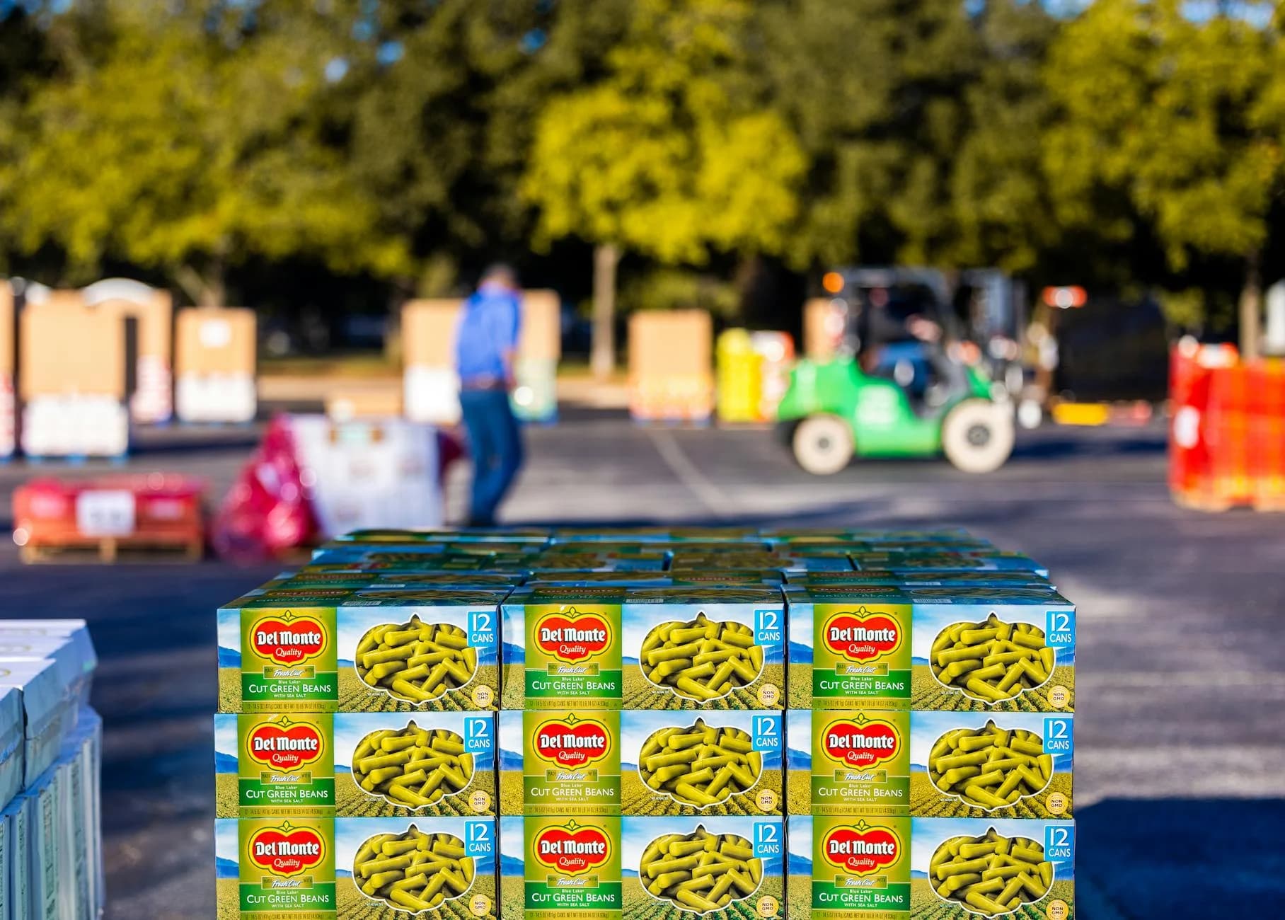 Stacked boxes of Del Monte green beans outdoors with forklifts in the background