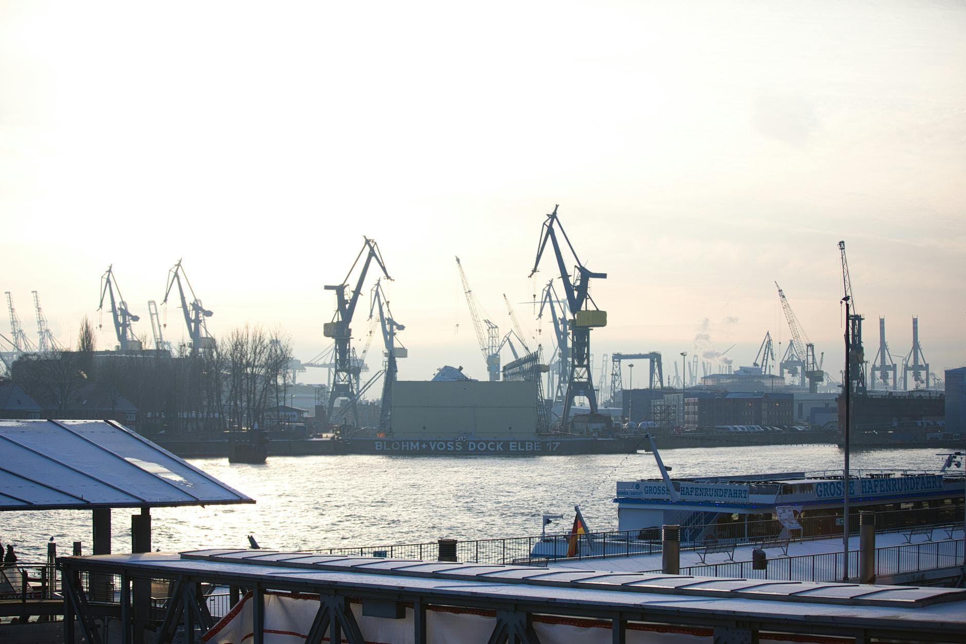 Silhouette of cranes in an Amsterdam harbor during sunset, creating a dramatic industrial scene.