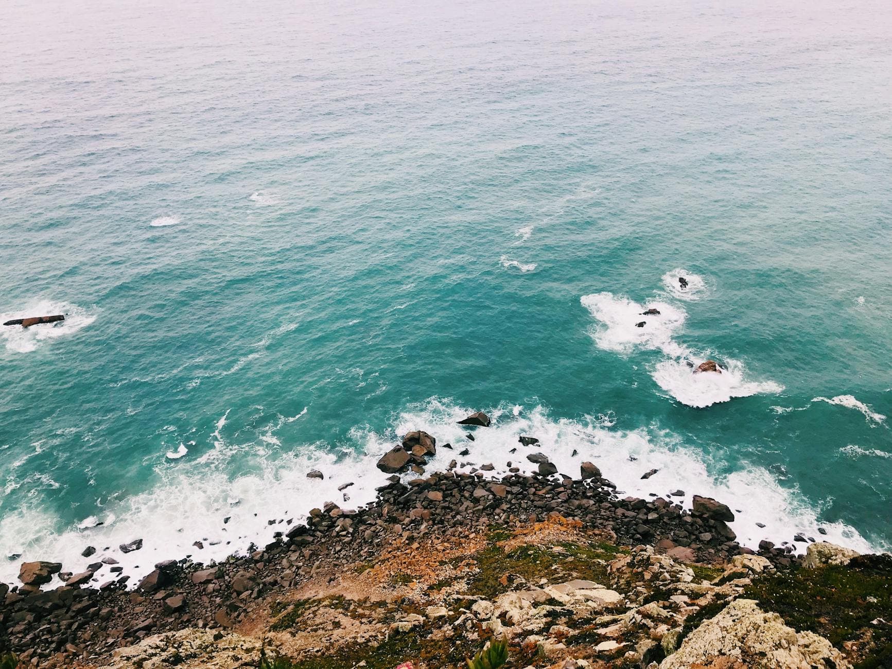 A stunning aerial view of the rocky coastline in Portugal with turquoise waves crashing against the shore.