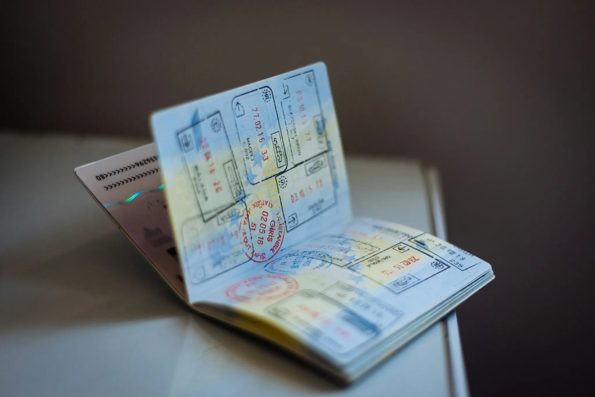 An open passport rests on a table, its pages filled with numerous international travel stamps and entry visas. The soft, ambient lighting highlights the texture of the document and creates a reflective, slightly nostalgic mood evocative of past journeys.