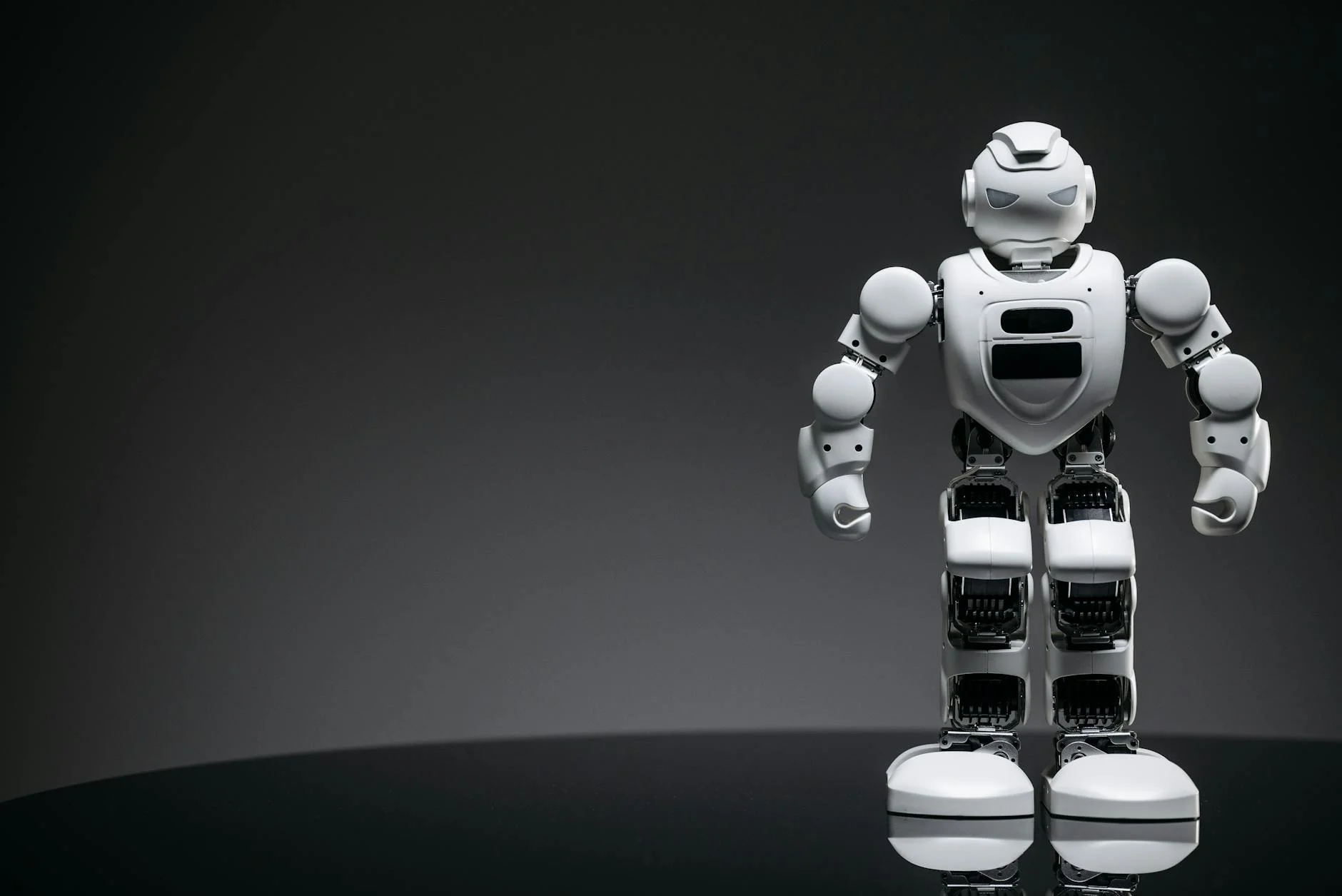 Close-up of a white toy robot on a reflective surface with dark background.