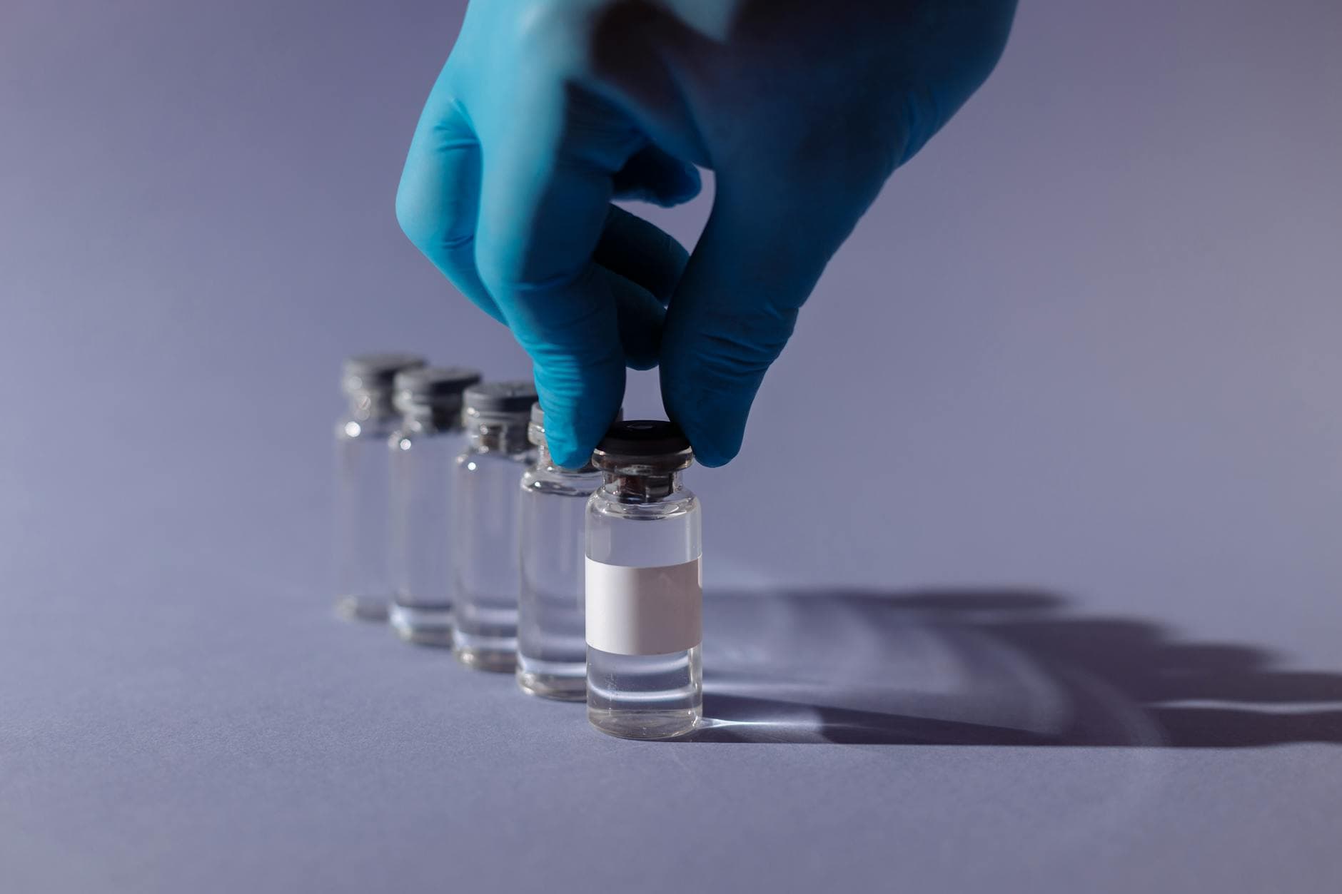 Healthcare worker with gloves handling vaccine vials in a sterile environment.