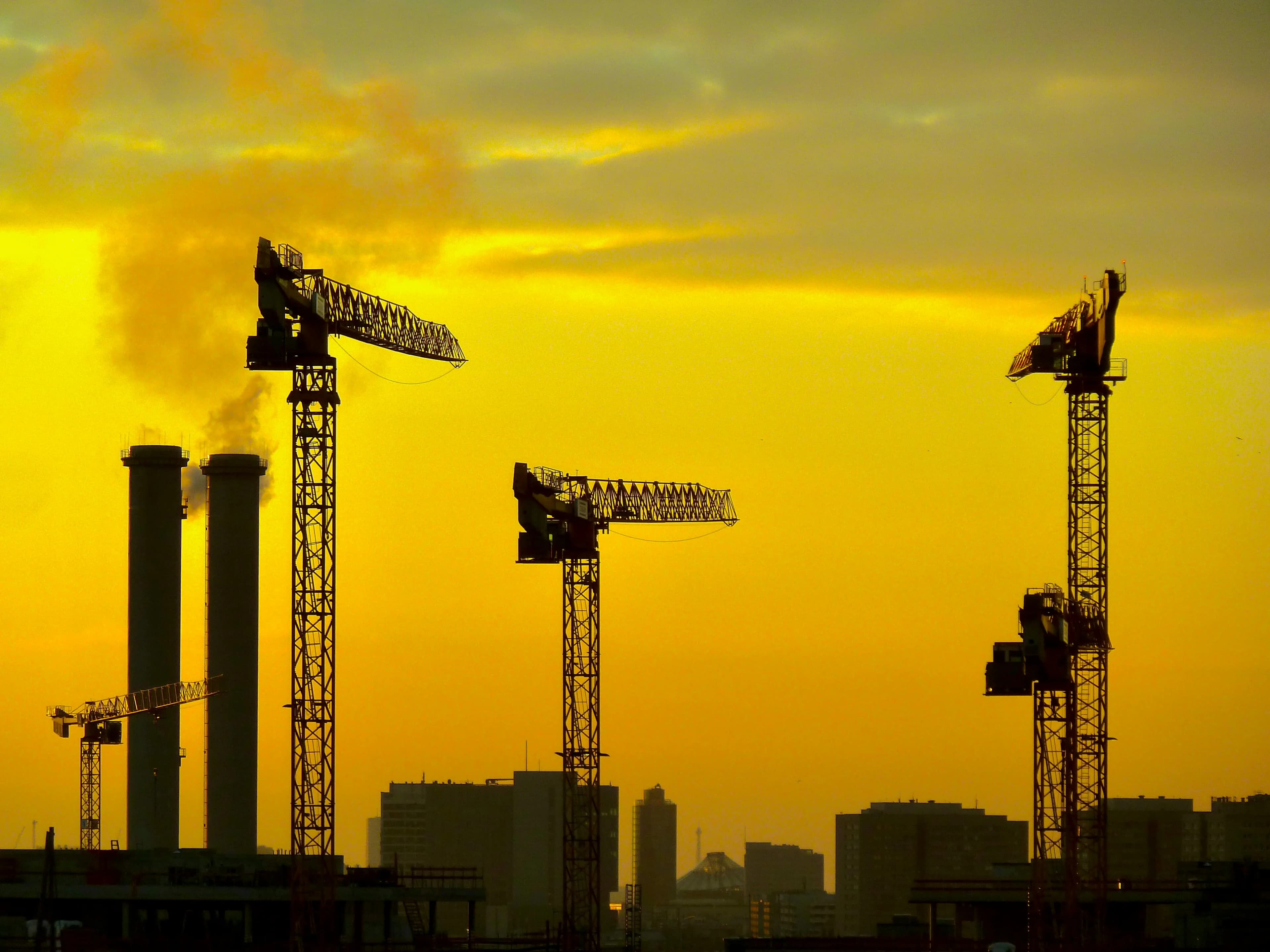 Construction cranes silhouetted against a vibrant sunset sky.