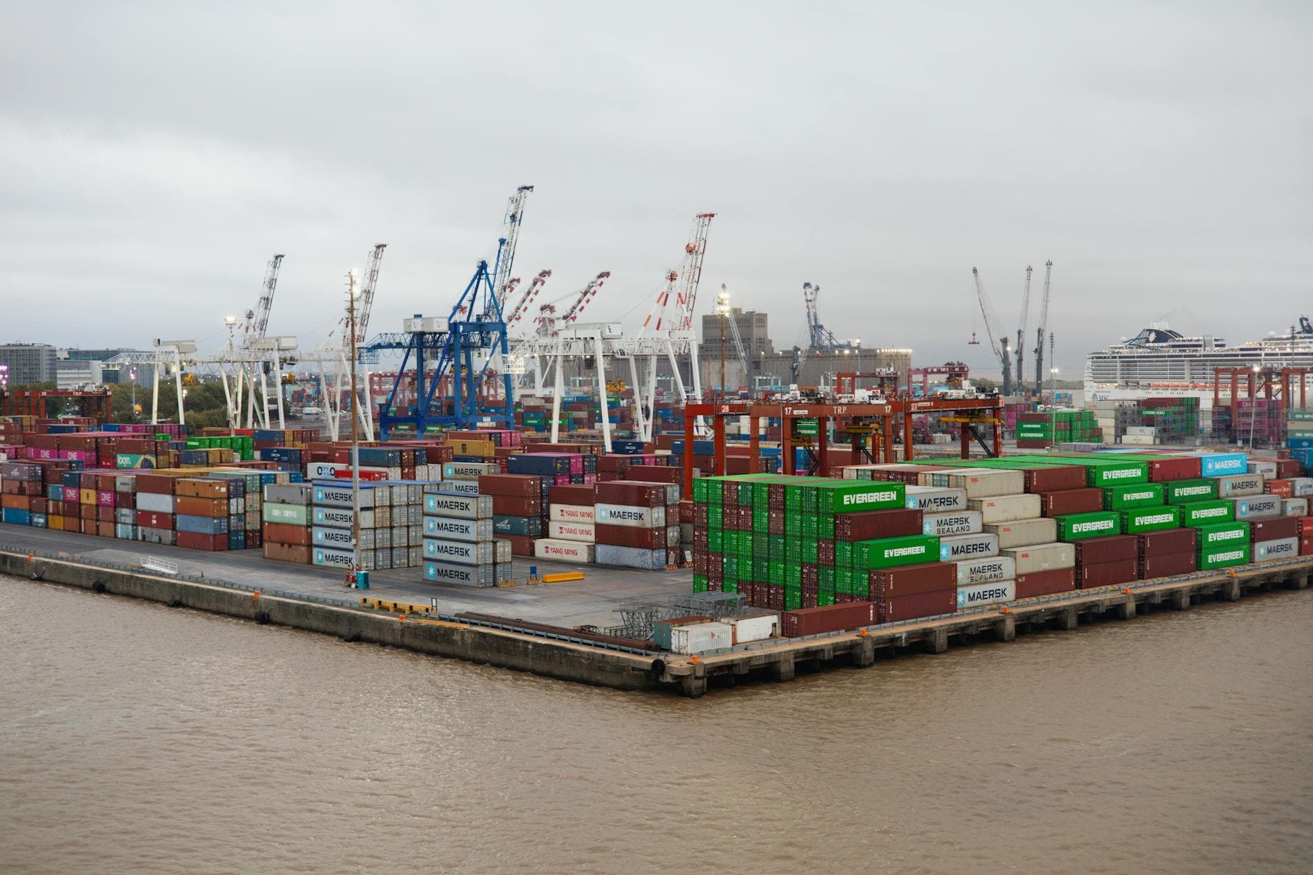 A bustling shipping port with stacked cargo containers and cranes under overcast skies.