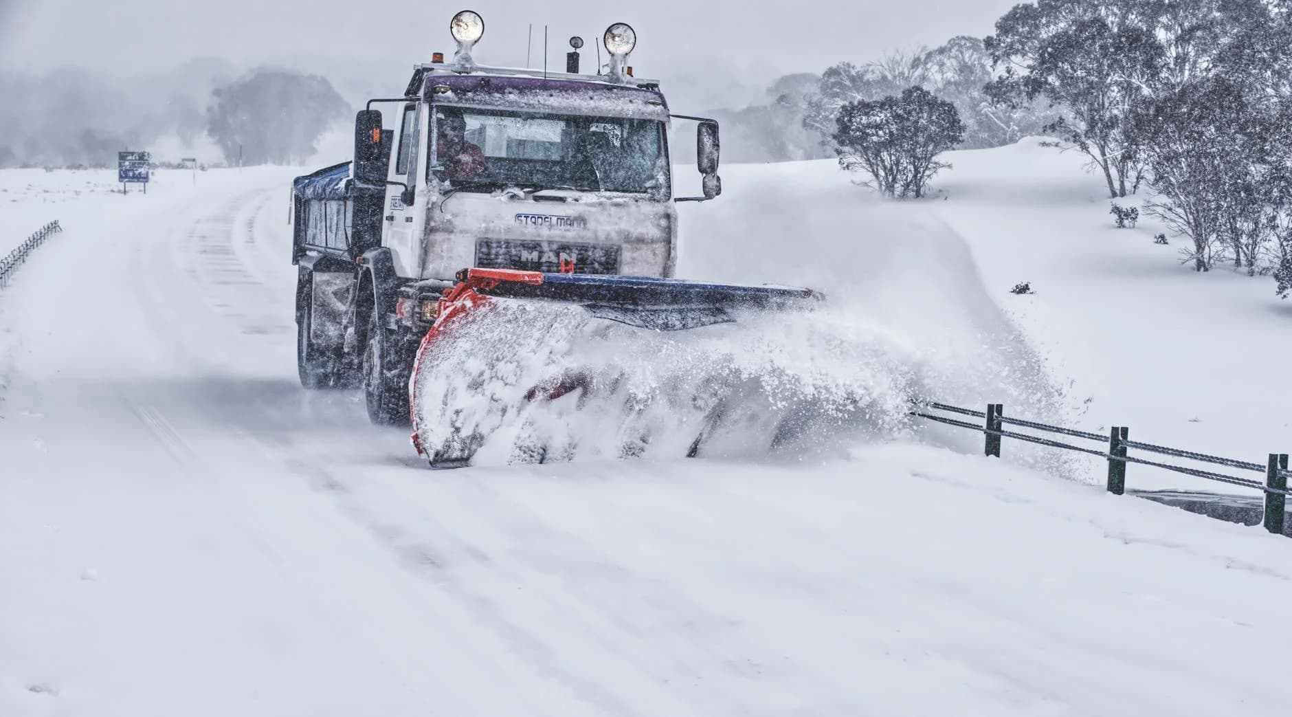 A powerful snow plow truck clearing a snow-covered road in a serene winter landscape.