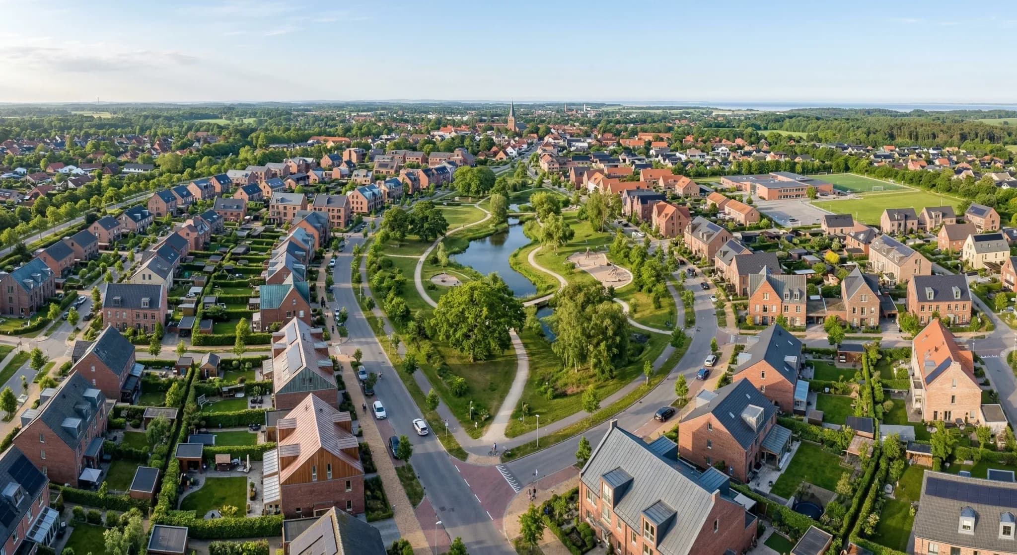 A photorealistic aerial view of a European suburban neighborhood, showing a mix of modern brick residential buildings and integrated green park areas. The scene is captured in soft, natural morning li