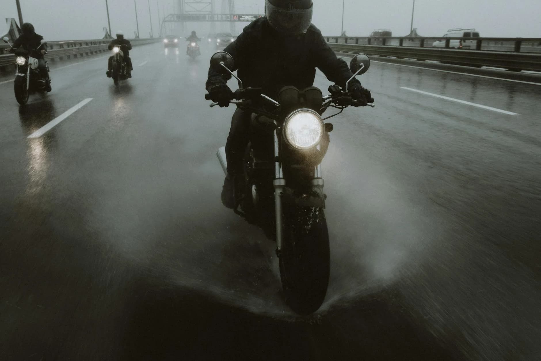 Group of motorcyclists riding in the rain on a highway, creating dynamic splashes.