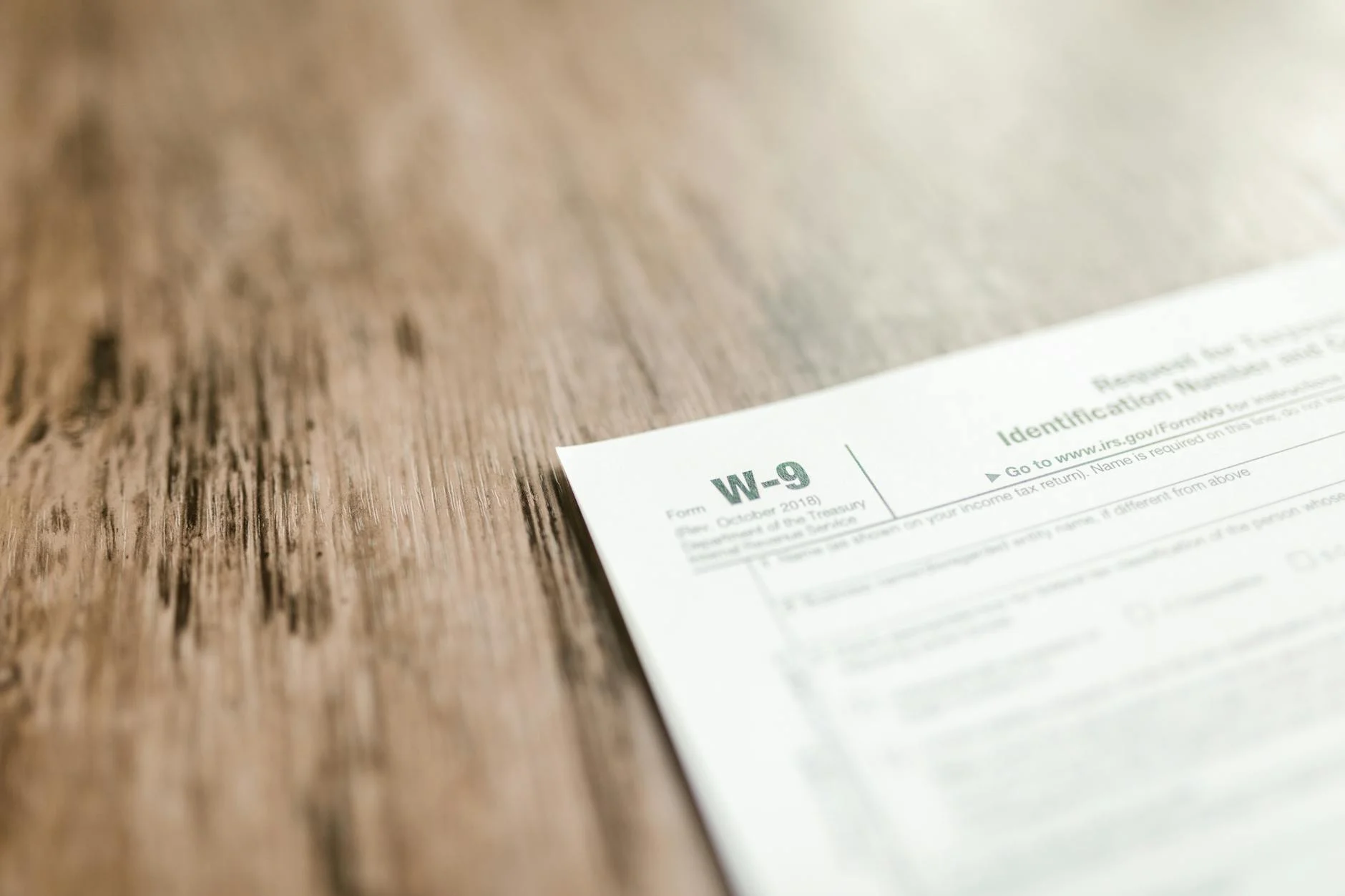 A close-up of a W-9 tax form placed on a wooden desk, emphasizing paperwork and finance.