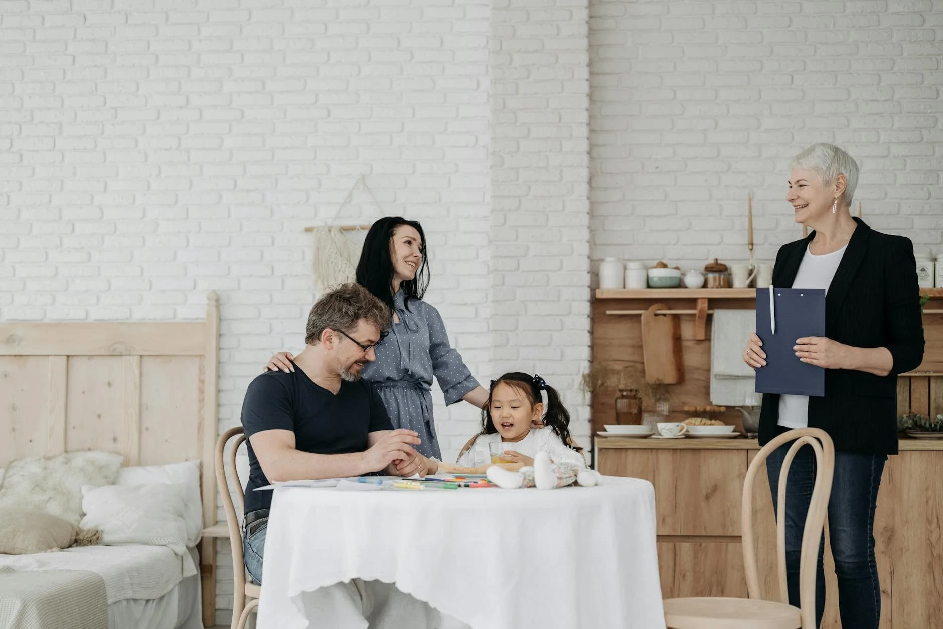 A happy family sits at a table with a child and social worker indoors, symbolizing adoption or foster care.