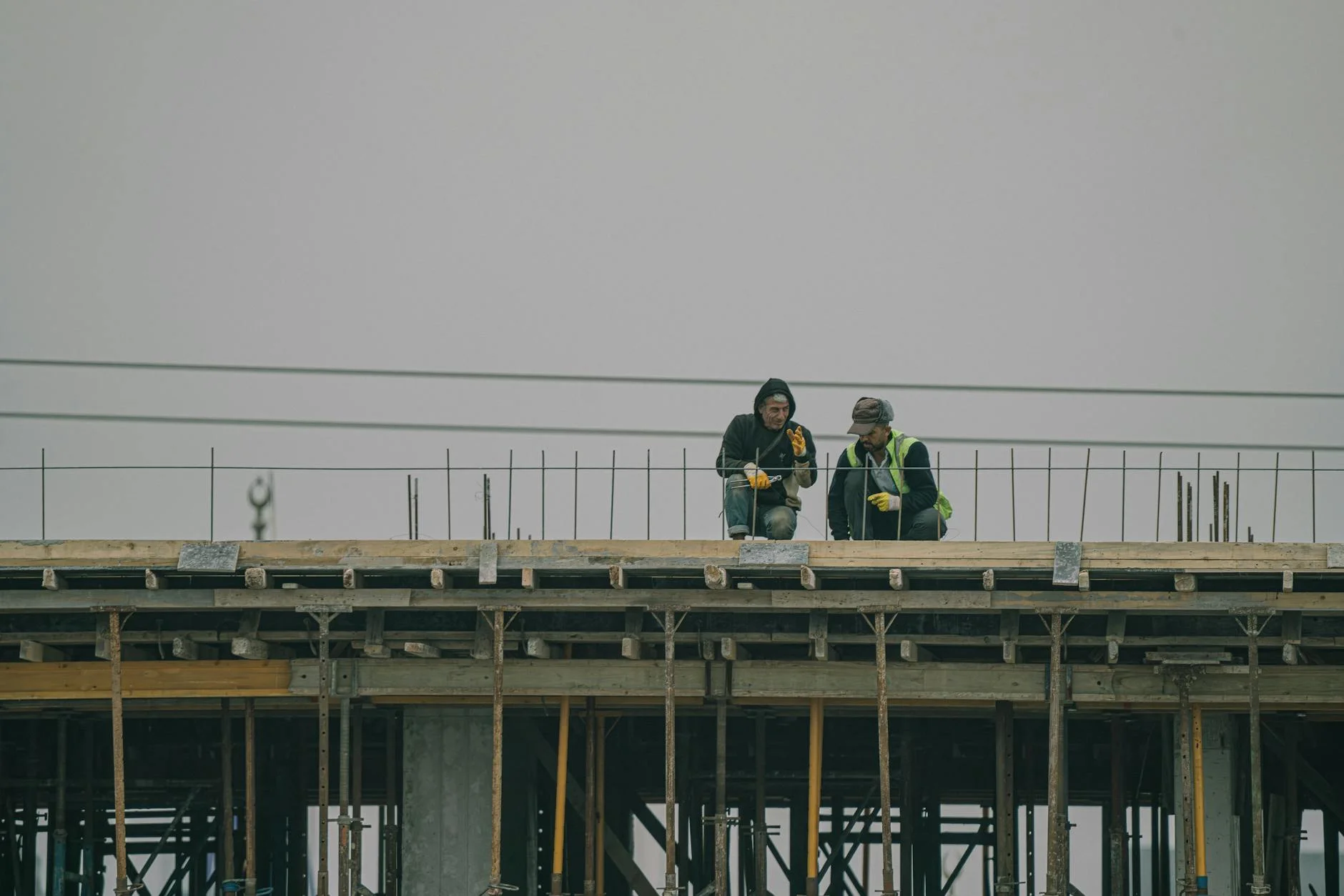 Two construction workers on a building site in Denizli, Türkiye, working under overcast skies.