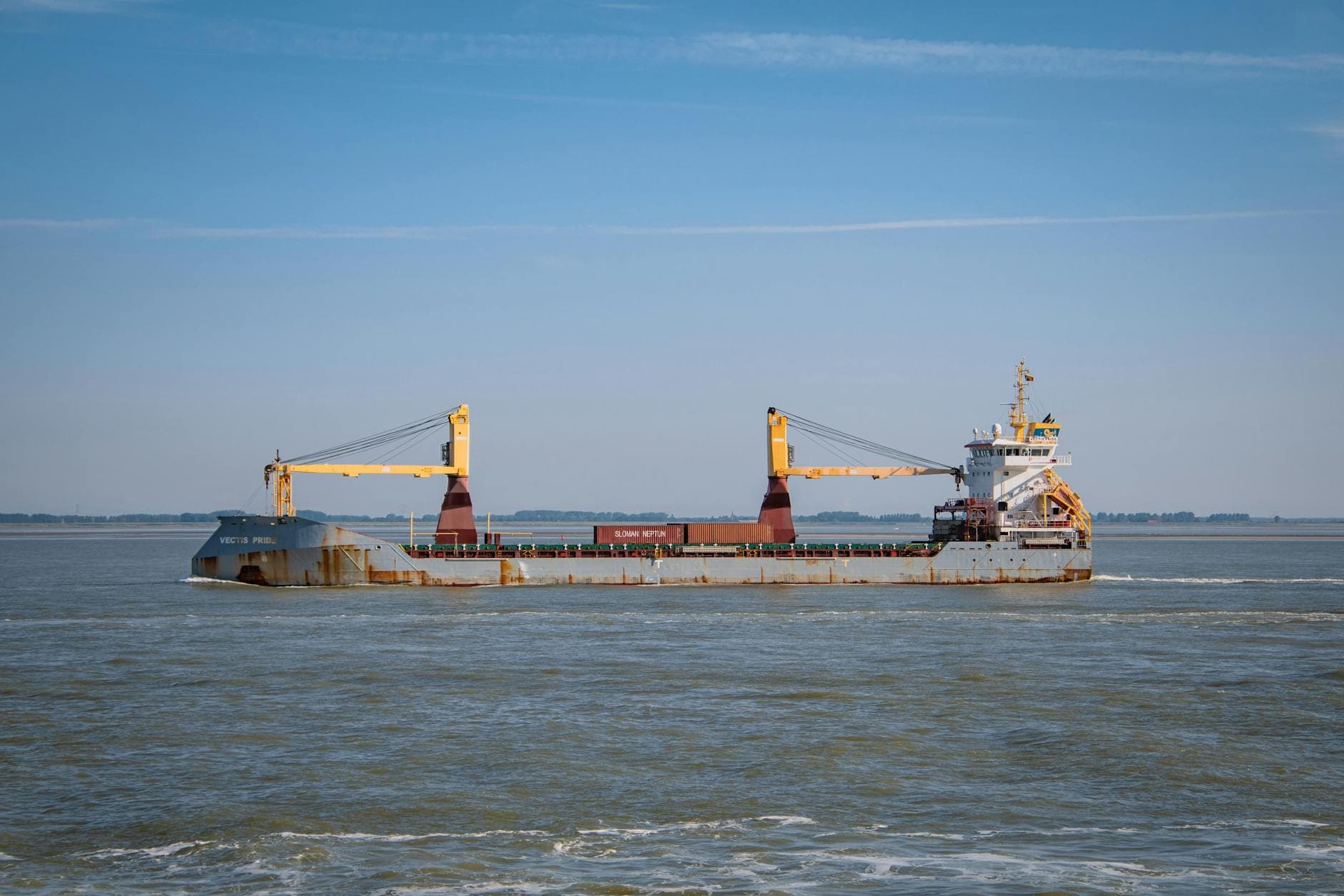 Cargo vessel carrying containers off the coast of Terneuzen in the Netherlands under a clear blue sky.