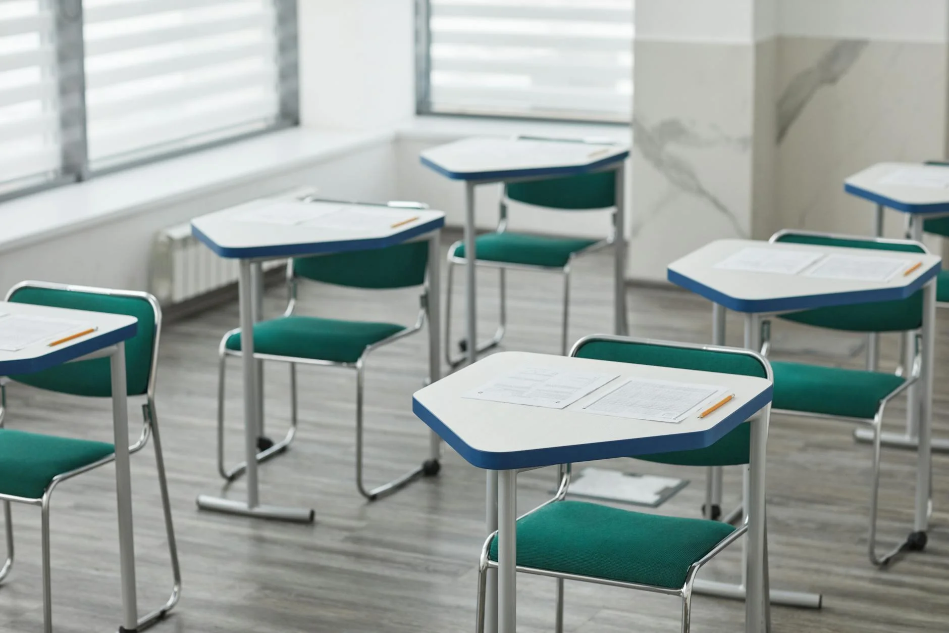 An empty classroom with arranged desks, exam papers, and pencils ready for students.