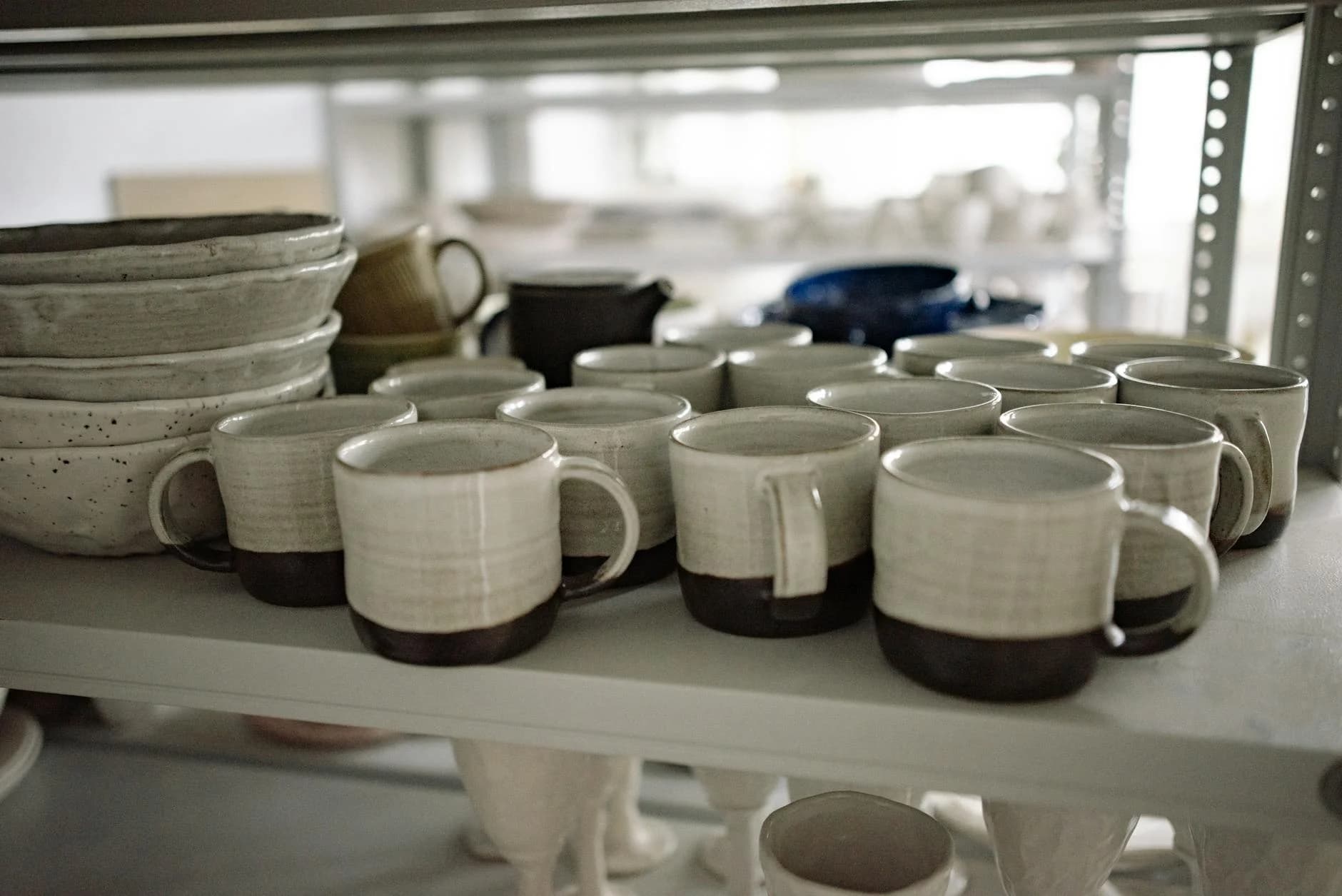 Close-up of artisan-crafted ceramic mugs on a shelf, showcasing pottery craftsmanship.