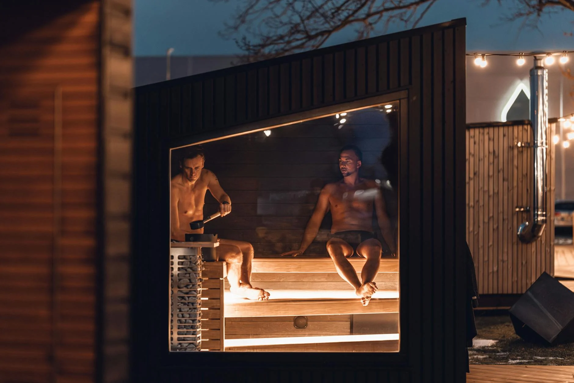 Two men relax in a modern Nordic sauna cabin, enjoying a tranquil evening.