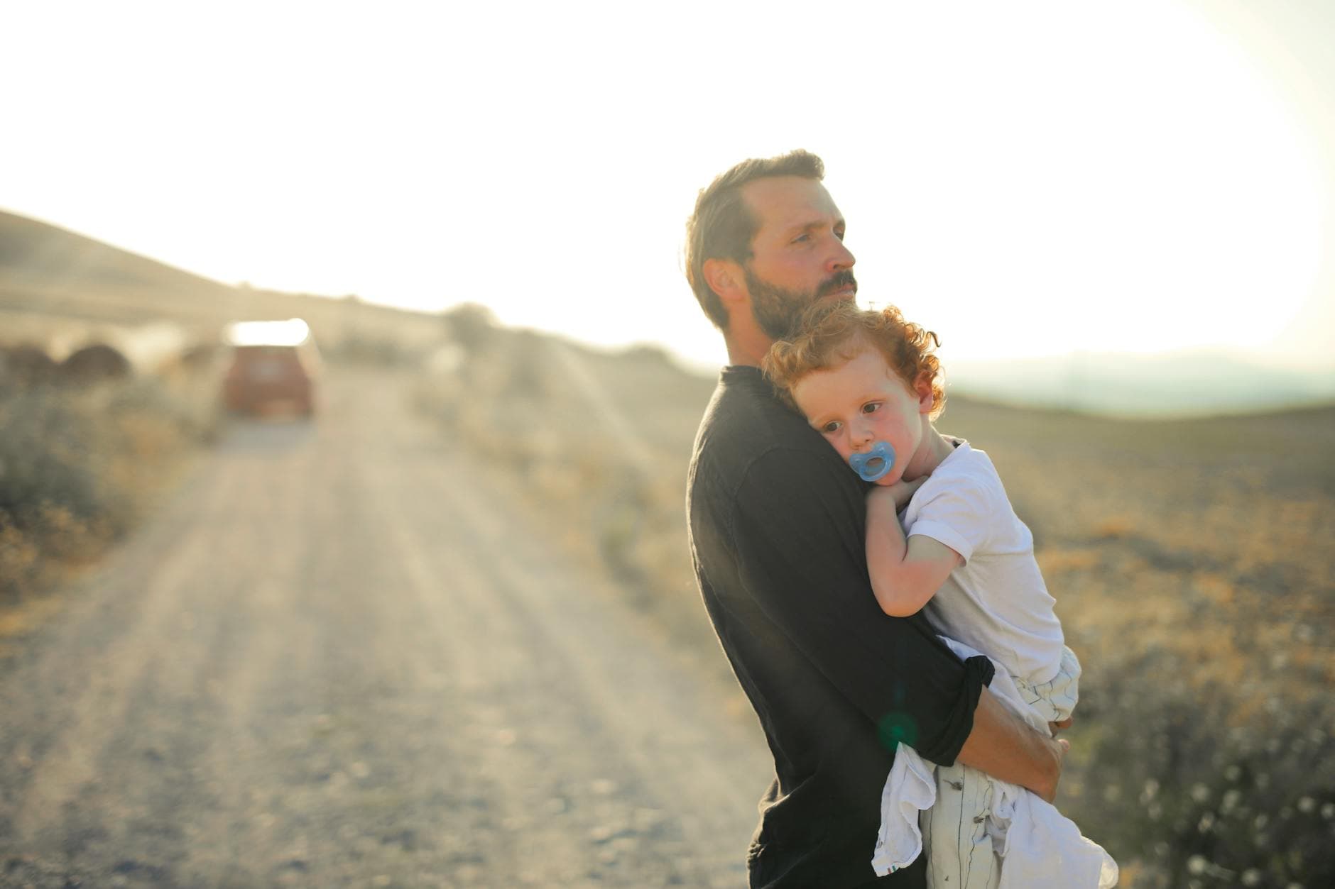 A father lovingly holds his child on a rural road at sunset, symbolizing family bonding.