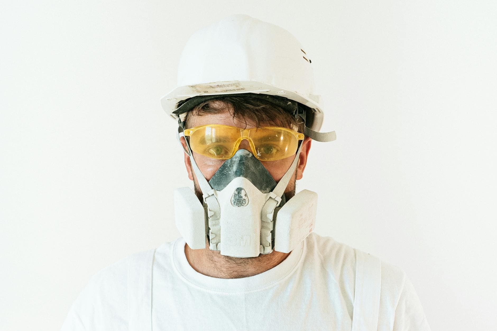 Close-up of a construction worker wearing a hard hat, safety goggles, and respirator mask against a white background.
