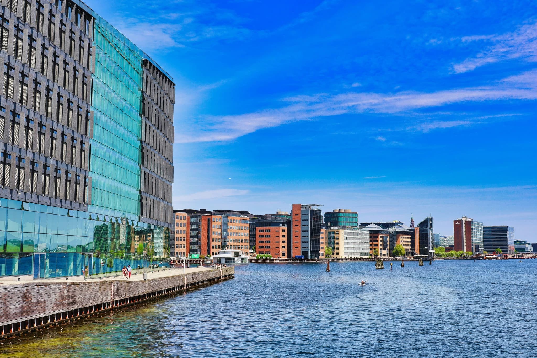 Modern buildings along a waterfront under a blue sky.