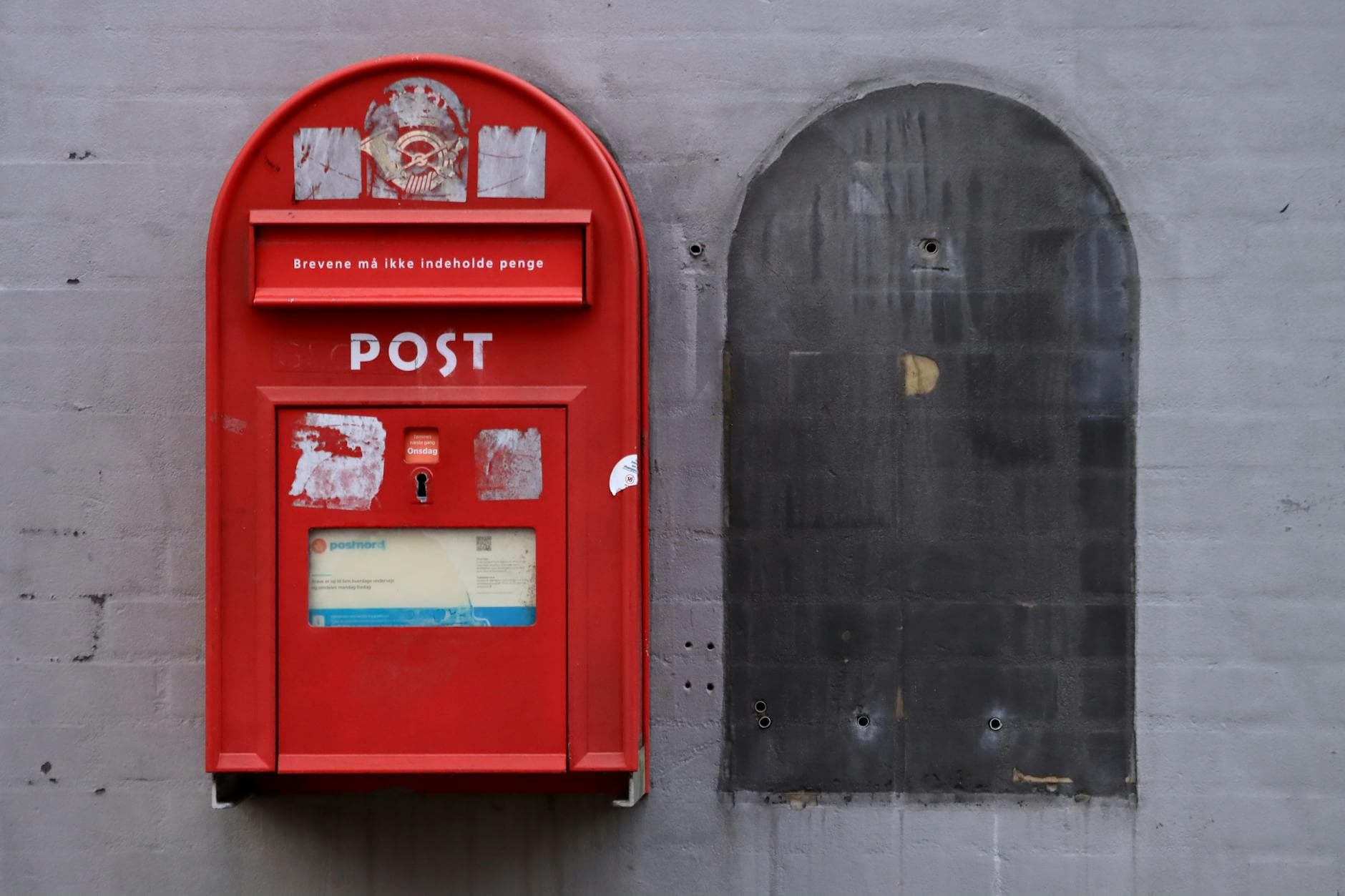A classic red post box mounted on an urban gray wall with historical details.