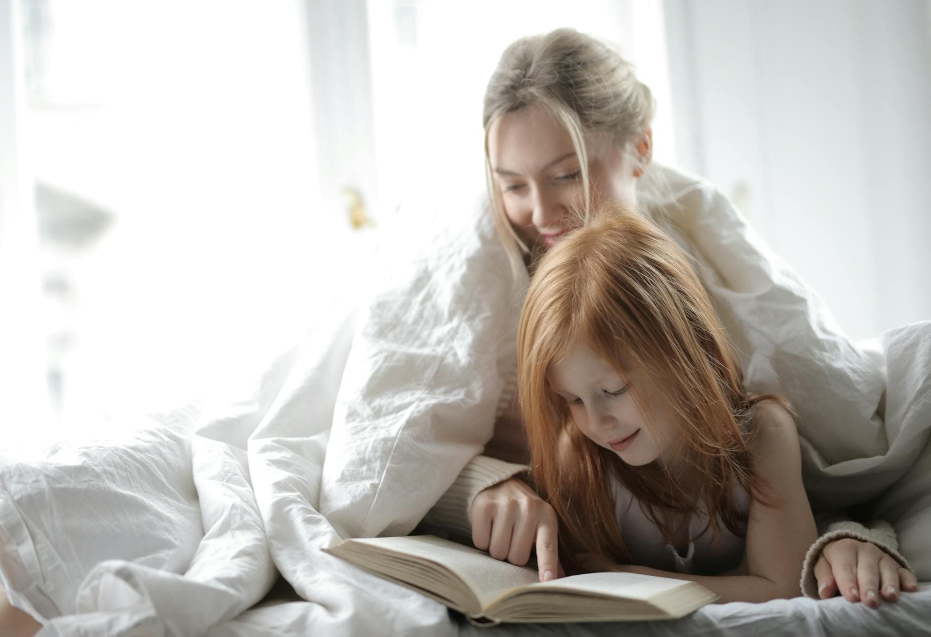 Loving mother and daughter reading a book together in bed, enjoying quality time and warmth.