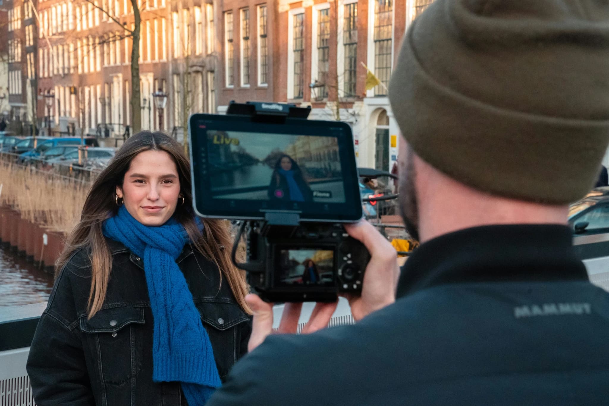 Man films woman by canal with buildings