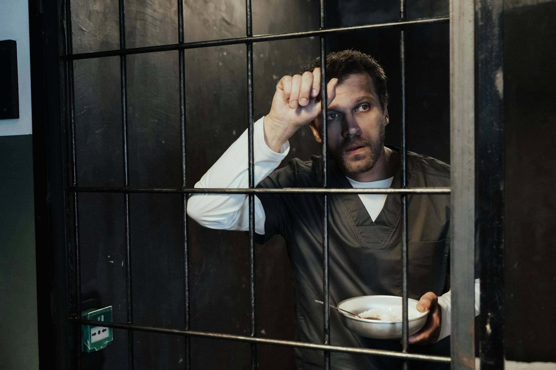 Portrait of a man in a prison cell holding a bowl, depicting confinement.