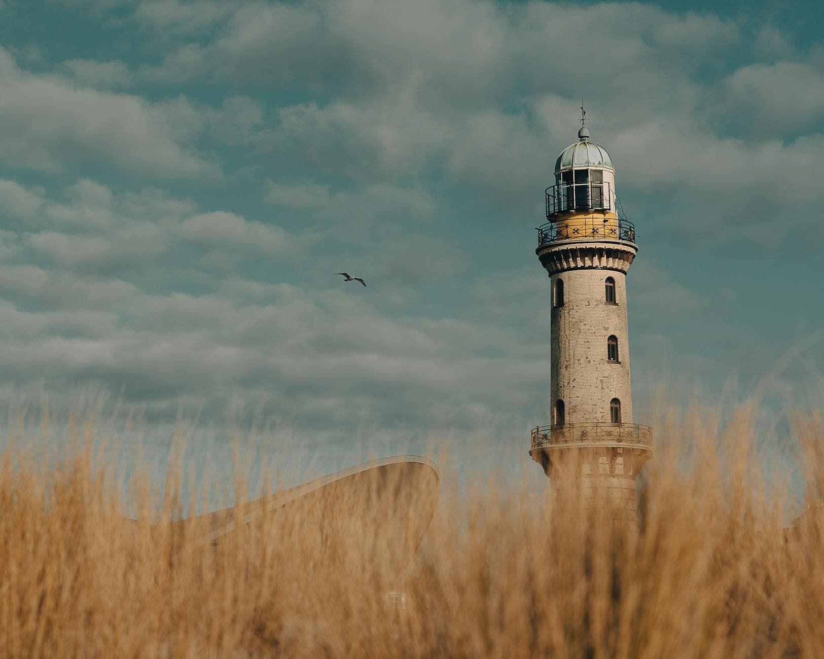 Scenic view of Warnemünde Lighthouse with a seagull flying nearby against a cloudy sky.