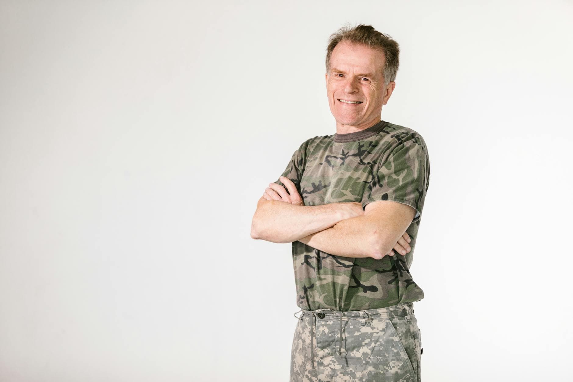 Smiling military veteran confidently posing in camouflage against a white background.