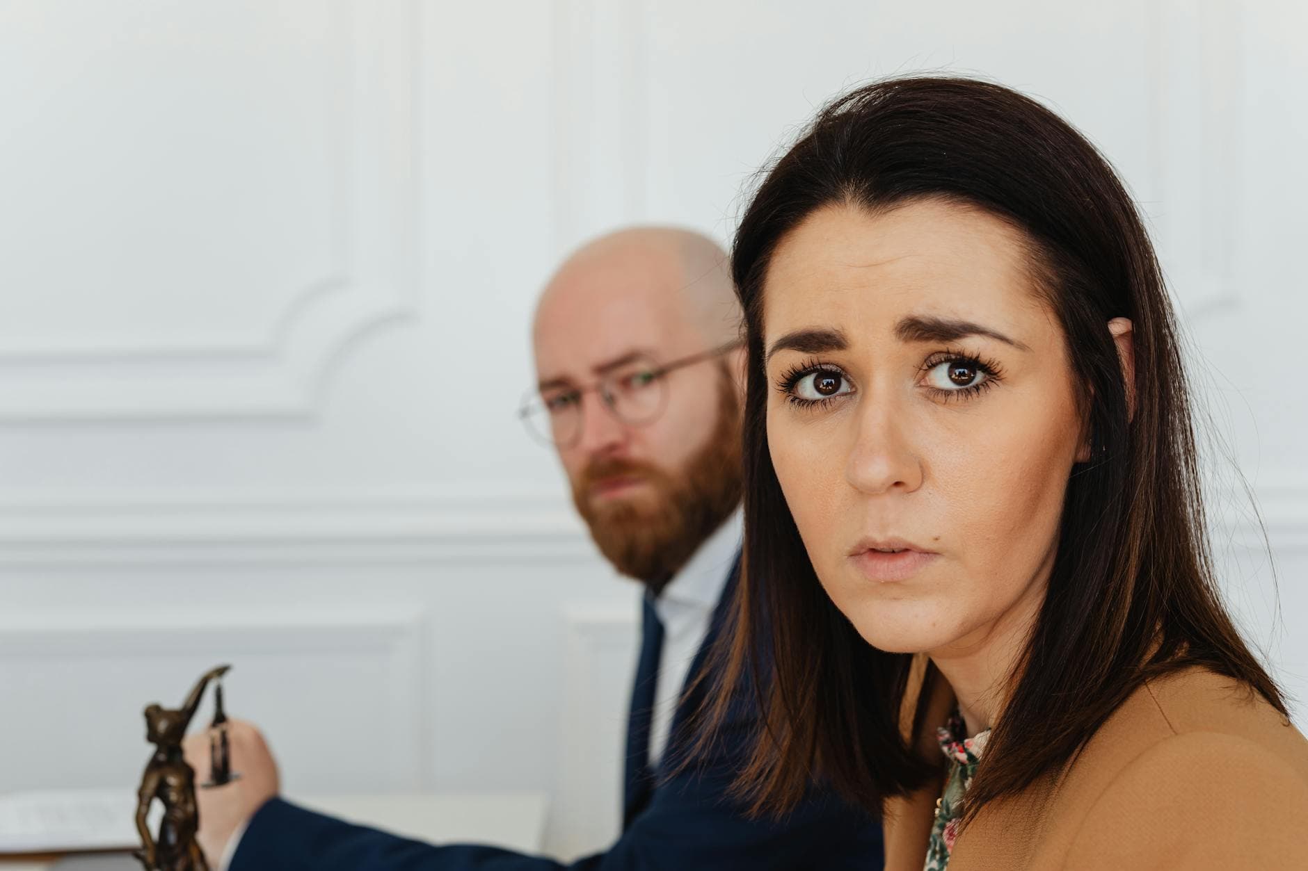 A concerned woman in an office setting, with a colleague in the background, depicting workplace tension.