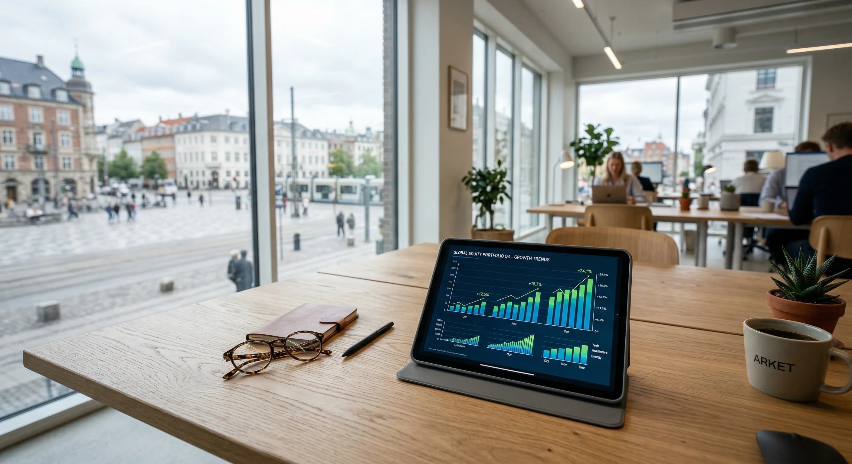 A close-up, wide-angle shot of a clean oak desk in a Scandinavian-style office. In the foreground, a modern tablet displays a professional financial chart showing rising trends, with a pair of reading
